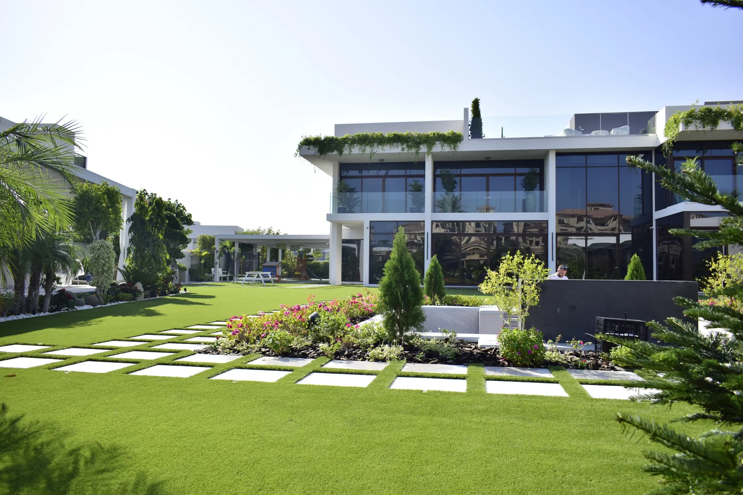 Naples 42 mm artificial grass running between mature trees, clipped topiary and stone paving in the garden of a villa on Saadiyat Island, Abu Dhabi.