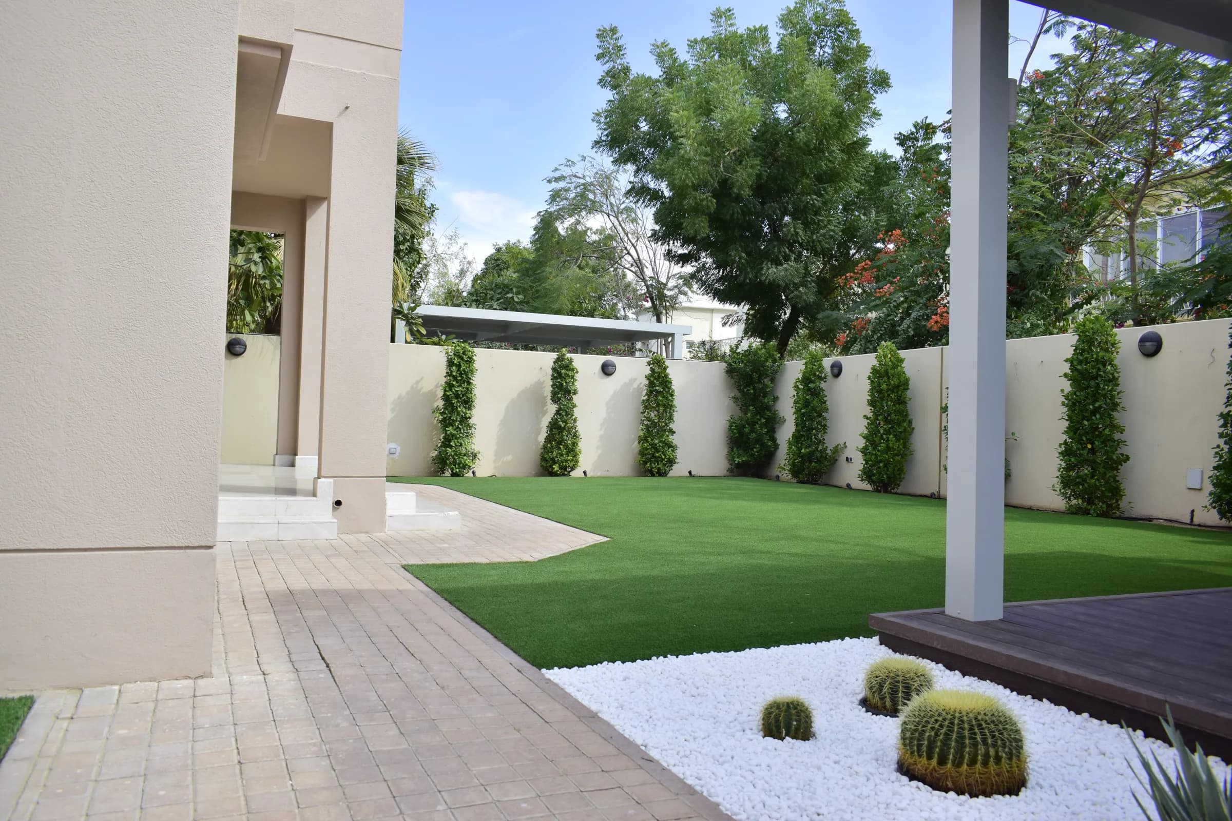 Artificial grass running to a clean paved edge beside a villa terrace and timber decking in Dubai.