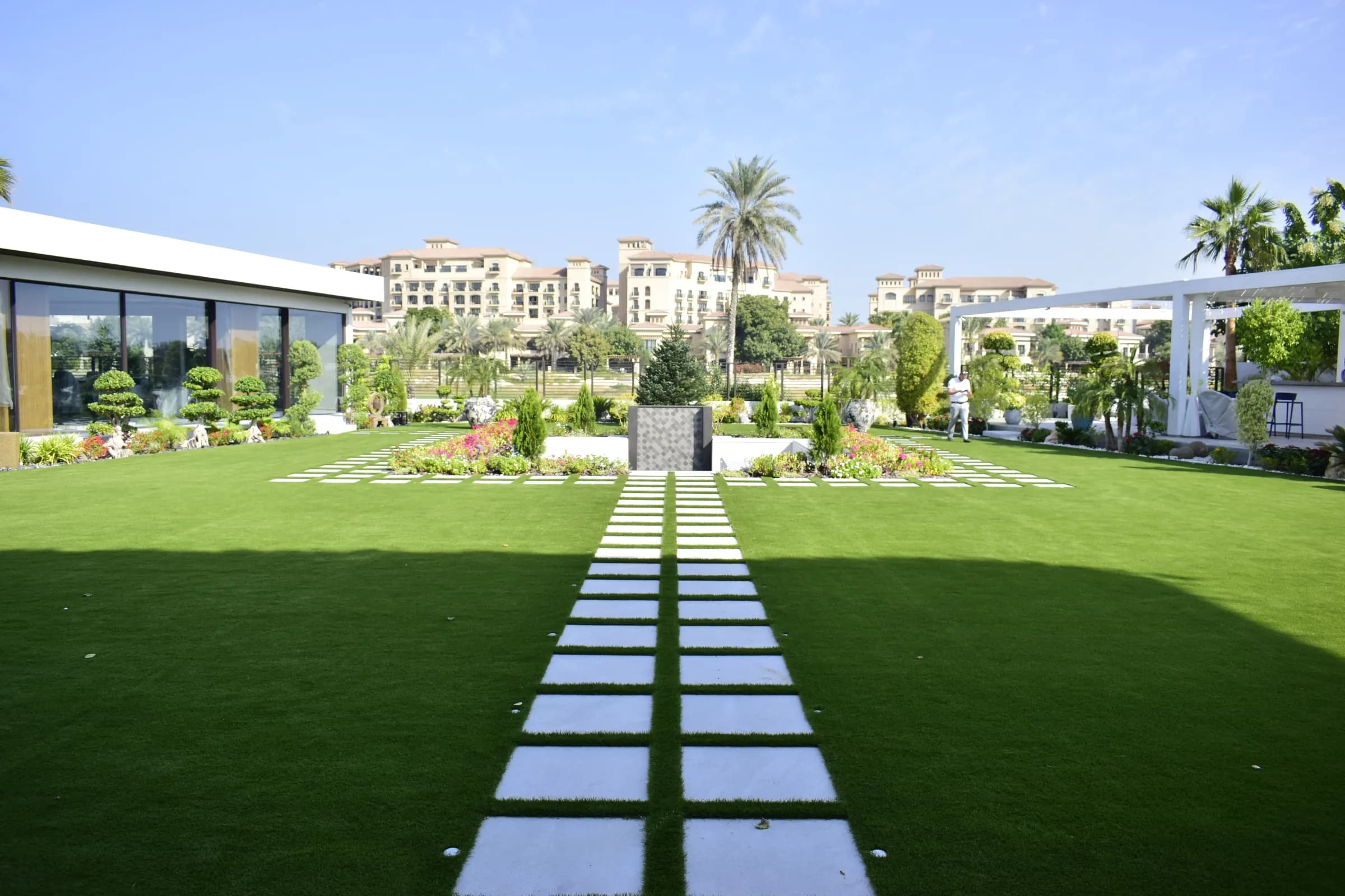 A large landscaped garden on Saadiyat Island with artificial grass laid around stone stepping slabs, clipped topiary and planting beds.
