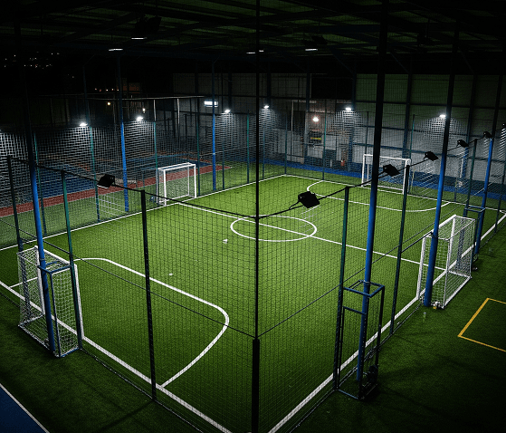 Indoor caged five-a-side Maze football pitch under floodlights at night
