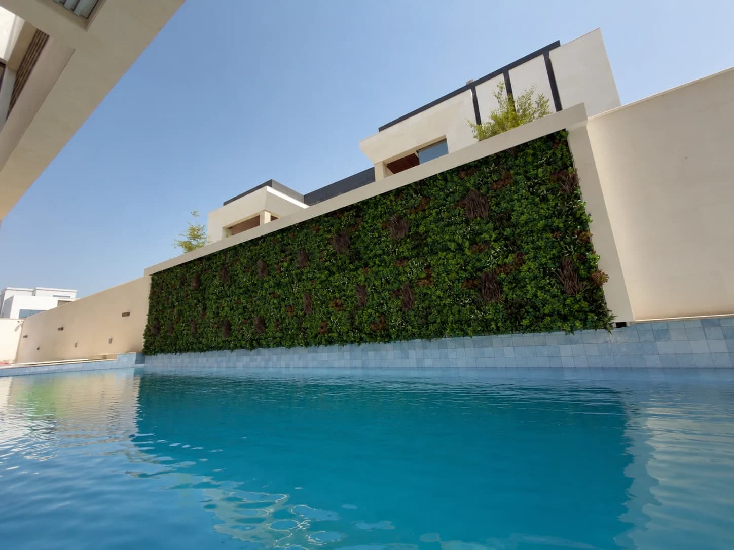 An artificial green wall of mixed foliage panels running the full height of a poolside wall, with water in the foreground.